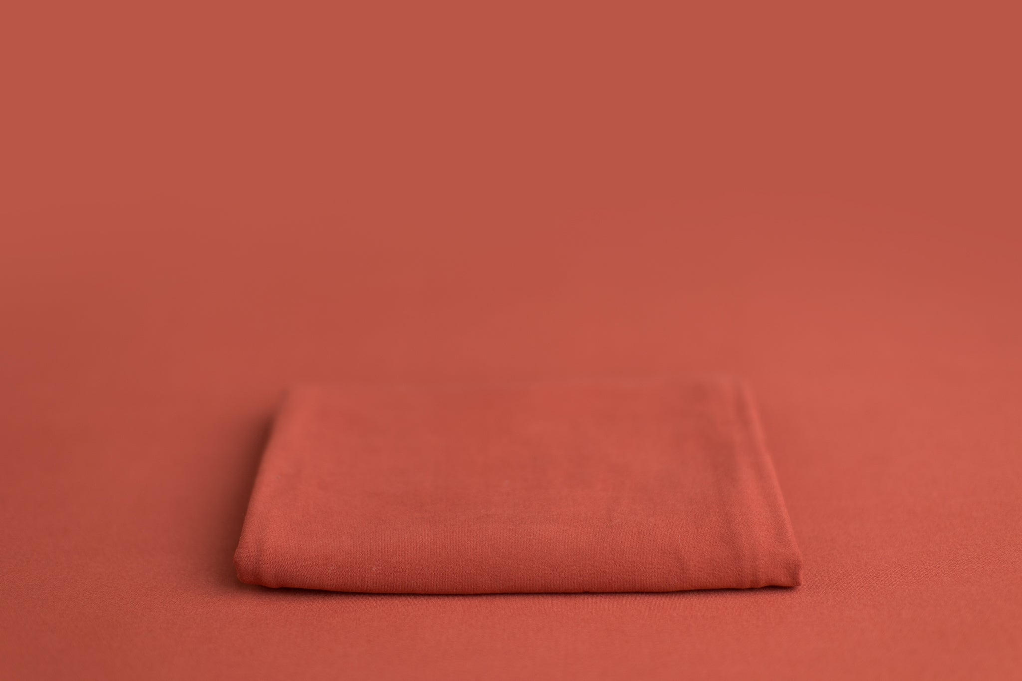 Chandler Rouge a deep pink leaning orange newborn photography backdrop draped on a posing table or beanbag, that is a smooth, stretchy and soft fabric for beautiful baby portraits.