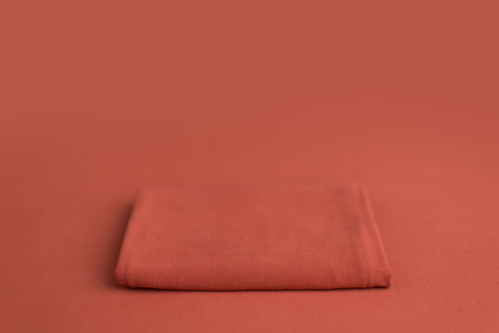 Chandler Rouge a deep pink leaning orange newborn photography backdrop draped on a posing table or beanbag, that is a smooth, stretchy and soft fabric for beautiful baby portraits.