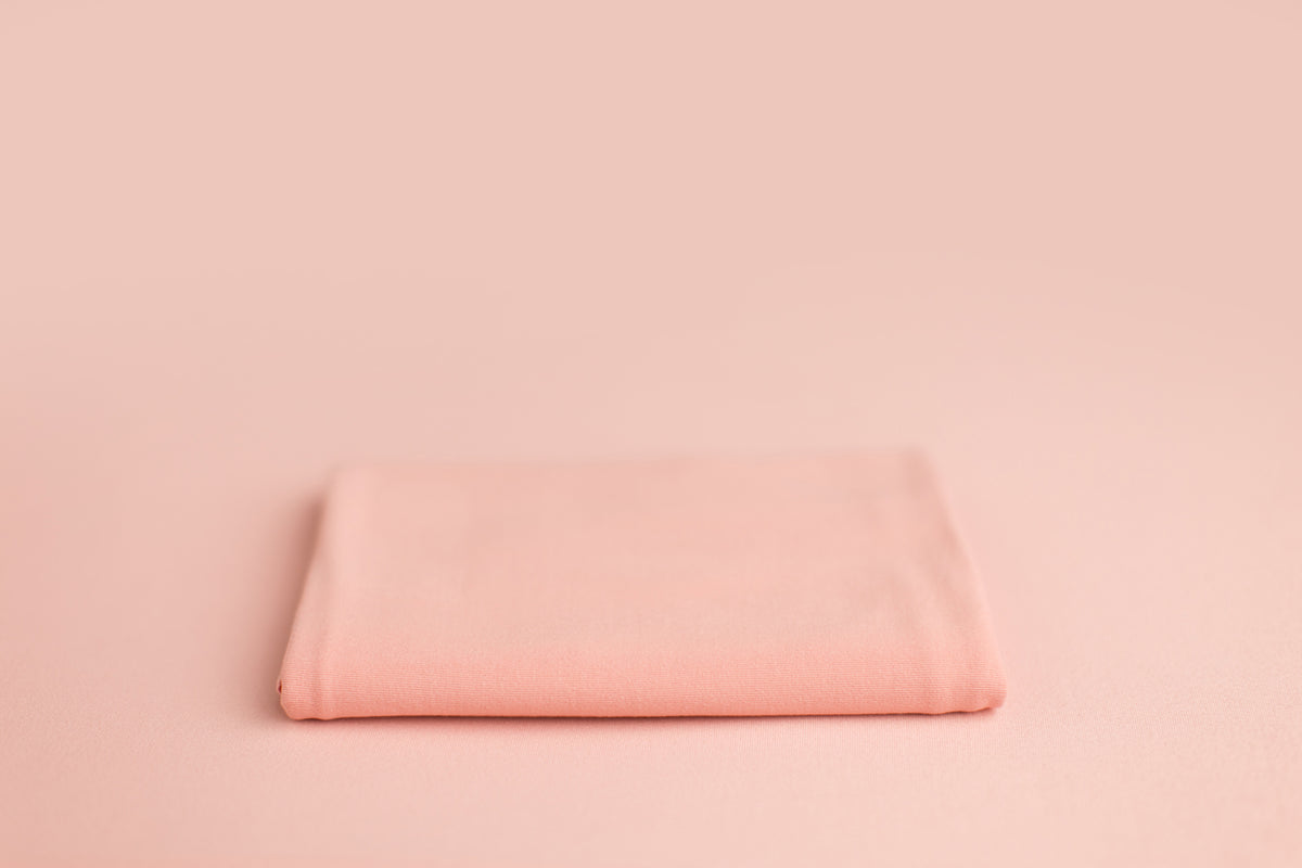 Chandler Shrimp a light pink newborn photography backdrop draped on a posing table or beanbag, that is a smooth, stretchy and soft fabric for beautiful baby portraits.